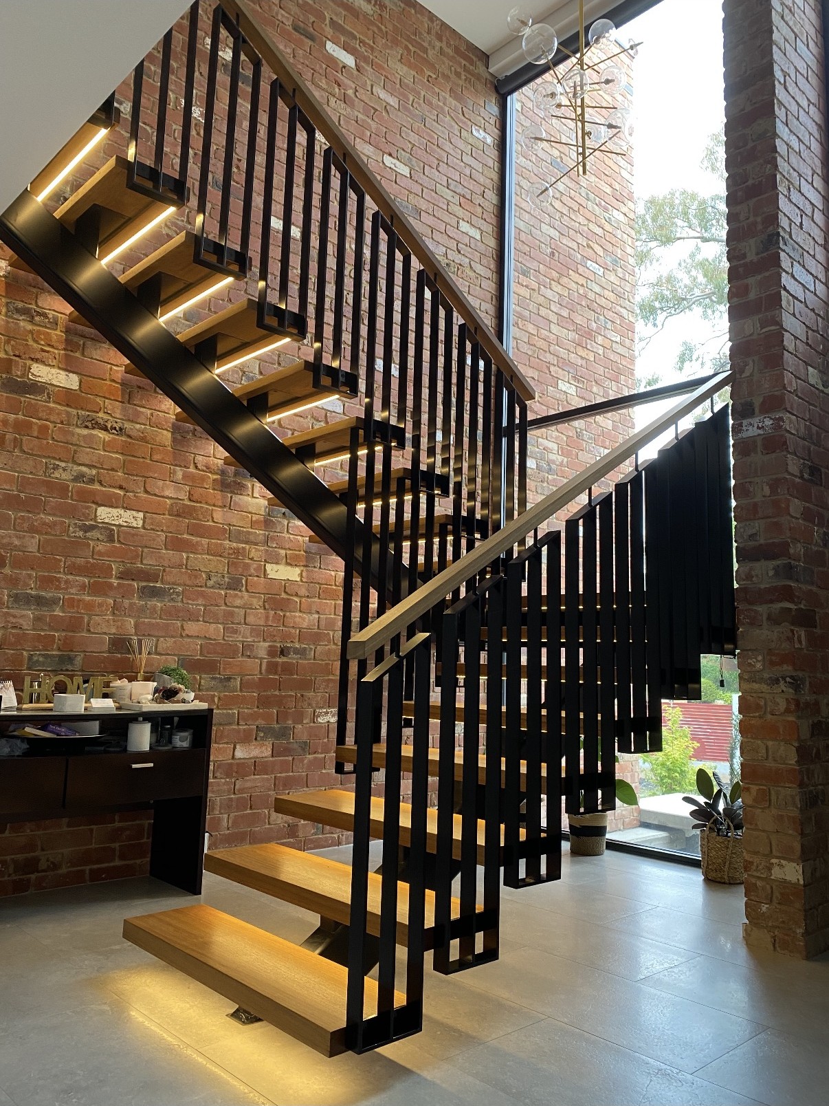 Steel and timber staircase with LED-lit treads against an exposed brick wall